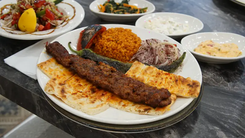 Lavaş üstünde Adana kebap, bulgur pilavı, közlenmiş biber ve sumaklı soğan